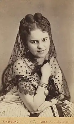 Photographie d'une jeune femme aux cheveux épinglés, portant une robe blanche et un foulard partiellement transparent.