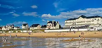 Plage et maisons en bord de mer. Des individus se promènent sur la plage.