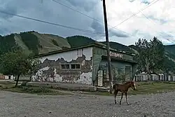 Poulain oux très foncé devant un bâtiment délabré.