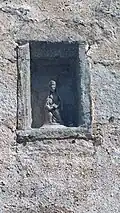 Photographie d'une niche de façade en granit, contenant une statuette.