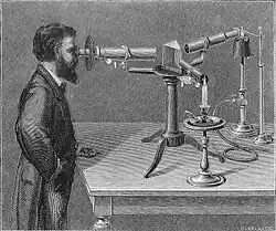 Image ancienne représentant un homme barbu devant un spectroscope ancien dont on voit le prisme et la bougie.