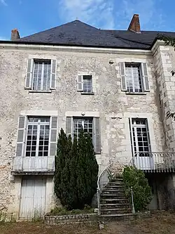 Photographie en couleurs d'un bâtiment dont la porte s'ouvre à l'entresol par un escalier en façade.