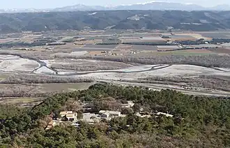 Hameau de pavillons modernes, au milieu des chênes verts, sur un promontoire dominant la vallée de la Durance, plate et découpée de champs carrés. Au fond, le plateau de Valensole ondulé et sombre.