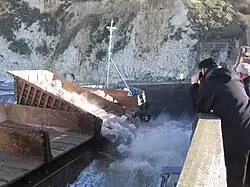 Inclinées, les bennes laissent tomber les roches qui s'amoncellent, elles formeront bientôt un nouveau talus amortisseur de houle placé contre l'épi qui supporte l'estacade.