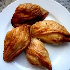 La photographie couleur présente une assiette blanche garnie de quatre pastizzi rôtis. Les stries apparentes montrent bien qu'il s'agit de pâte feuilletée.