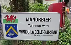 Photo d'un panneau blanc portant une inscription en anglais illustrée avec le drapeau gallois et le blason de Vernou-la-Celle-sur-Seine