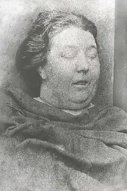 Photographie mortuaire en noir et blanc du visage d'une femme bien en chair.