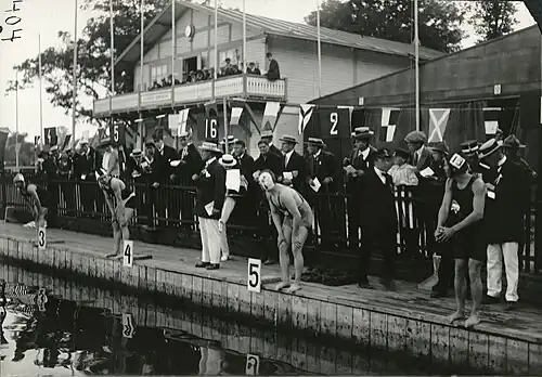 Photographie noir et blanc : quatre hommes au bord d'un bassin s'apprêtant à plonger