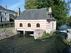 Photographie en couleurs d'un bâtiment dont la façade présente des lits alternés de pierre et de briques construit au dessus d'un cours d'eau.