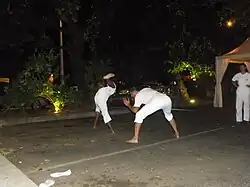 Le combat étant inévitable, le moringue utilise beaucoup les techniques de jambes. Ici un coup de pied circulaire esquivé par l'adversaire. On notera la recherche d'équilibre par un appui des mains au sol.