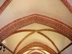 Photo couleur d'une voûte recouverte d'un enduit blanc sur lequel se détachent les arc-doubleaux et arêtes en brique rouge.