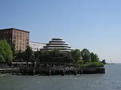 Photo en couleurs d'un bâtiment pyramidal et hexagonal émergeant au-dessus des arbres et d'un bras de mer