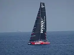 Bateau rouge progressant sous voiles noires par mer très calme.