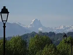 Photographie en couleurs d'une chaîne de montagnes enneigées en arrière-plan d'un paysage boisé.