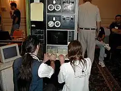 Deux personnes sont assises de dos et jouent à Spacewar! sur un vieil ordinateur ressemblant à une armoire.