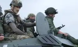 Photo de trois hommes casqués et masqués, assis sur le dessus d'un véhicule blindé.