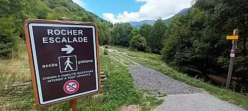 Photographie en couleur d'un panneau indiquant le sentier pour se rendre au rocher d'escalade.