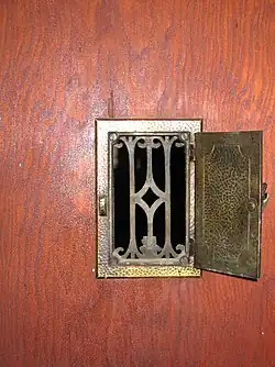 Une ouverture avec une grille de laiton ouvragée et un volet opaque