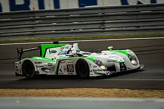 Photographie d'une voiture de sport-prototype blanche, verte et noire, vue de trois-quarts, sur une piste.