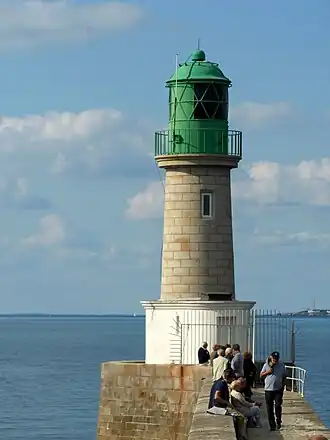 Vue d’un phare au bout d’une jetée, corps en granit et lanterne verte.