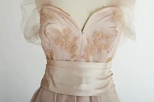 Une robe en satin rose avec une superposition de dentelle appliquée Carrickmacross avec un motif de papillon et de petites perles.
