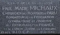 Photo de la plaque commémorative apposée sur la maison natale de Paul Michaux avec, pour inscription : « Ici est né le 16-11-1854 Paul Marie Michaux, Chirurgien des Hôpitaux de Paris Fondateur de la Fédération Gymnastique et Sportive des Patronages de France et de l’Union Jeanne la Lorraine et de l’U.I.O.C.P 19-6-1948 ».