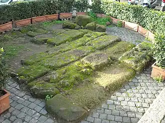 Photographie en couleurs d'un alignement de grands blocs de pierre dans une cour pavée.