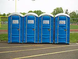 Quatre cabines de WC mobiles bleus posées le long d'un terrain de sport