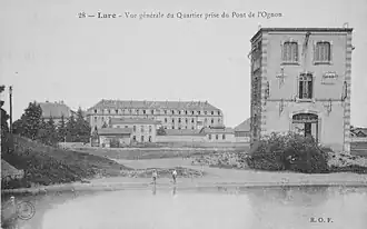 Photo noir et blanc montrant un bâtiment similaire mais avec des fenêtres plus arrondies, à l'arrière plan se trouve un haut bâtiment de caserne.