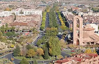 Photographie aérienne d'une avenue bordée d'arbres à la droite figure une église.