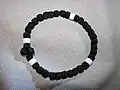 Tchotki en bracelet, avec trois séries de dix nœuds, séparées par des perles blanches, qui encadrent aussi la croix.