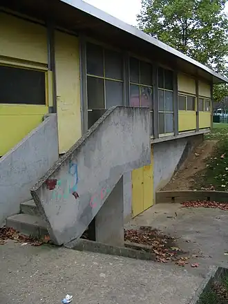 Photographie en couleurs représentant un bâtiment préfabriqué avec un escalier d'accès en béton au premier plan.