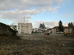 Un terrain vague avec chantier de construction et trois immeubles en fond, une tour et deux barres.