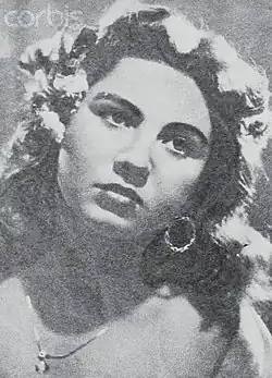 Image en noir et blanc, plein cadre d'un visage féminin, cheveux noirs bouclé, avec boucle d'oreille et collier.
