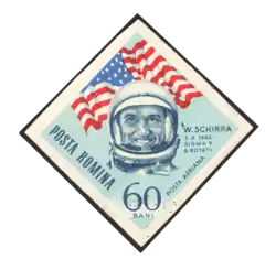 Scan d'un timbre roumain avec la tête casquée de Schirra devant un drapeau des États-Unis.