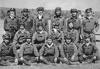 Photo noir et blanc d'un groupe d'hommes, pour la plupart en tenues de pilotes, debout, assis ou accroupis.