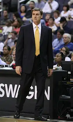 Portait de Rick Carlisle en costume noir et cravate jaune dirigeant son équipe du bord du terrain
