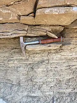 Un marteau-pic servant d'échelle sur la photographie d'un affleurement de métasédiments.