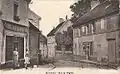 Vue dans la rue de l'église, l'actuelle rue Gaston Fouliouse, depuis la rue de la Liberté; de la boucherie-charcuterie à gauche et de l'épicerie-mercerie-pâtisserie à droite ne subsistent plus de traces.