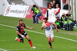 Joueur débordant sur le côté gauche du terrain, malgré l'arrivée d'un adversaire depuis son coté droit.