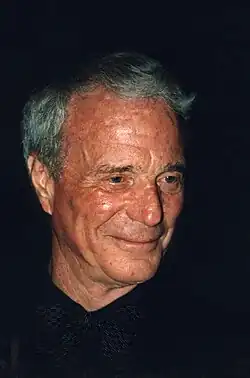 Gros plan sur le visage d'un homme âgé, portant une chemise et un nœud papillon noirs.