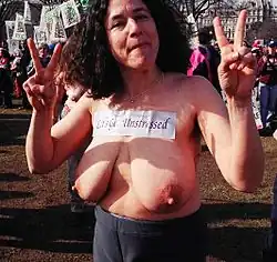 Sherry Glaser, de Breast Not Bombs, manifestant seins nus le 8 mars 2003 devant la Maison-Blanche avec l'écriteau Let's get Unstressed (déstressons-nous) qui se rapproche du Let's get undressed (déshabillons-nous).