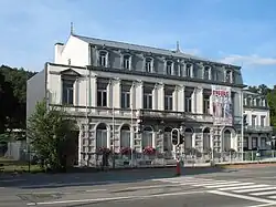 Bâtiment de style néoclassique à la façade en pierre et enduit comprenant neuf baies sur deux niveaux surplombés d'un étage mansardé en ardoises à sept fenêtres