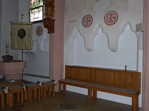 Photographie d'un banc de bois placé devant une triple niche creusée dans le mur d'une église.