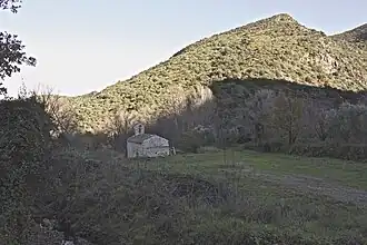 Petite église dans l'ombre. À l'arrière plan, une petite montagne éclairée par le soleil rasant.
