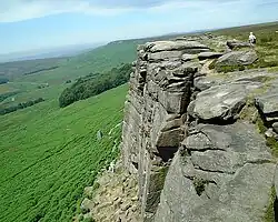 Au-dessus d'une pente raide et couverte de buissons, haute falaise grise formée de larges dalles