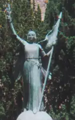 Statue de Jeanne d'ArcStatue en ange protecteur de la France, vêtue d'une robe et pourvue de deux ailes, drapeau à hampe piquée à la main, et épée au fourreau, avec un bas-relief sur le socle.