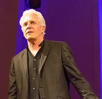 un homme aux cheveux blancs, avec un costume noir