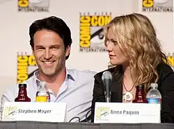 Un homme brun et une femme blonde, souriant derrière des micros.