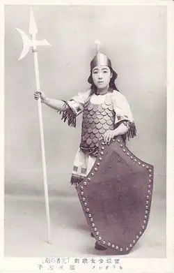 Carte postale en noir et blanc représentant une femme déguisée en soldat, armé d'une hallebarde.